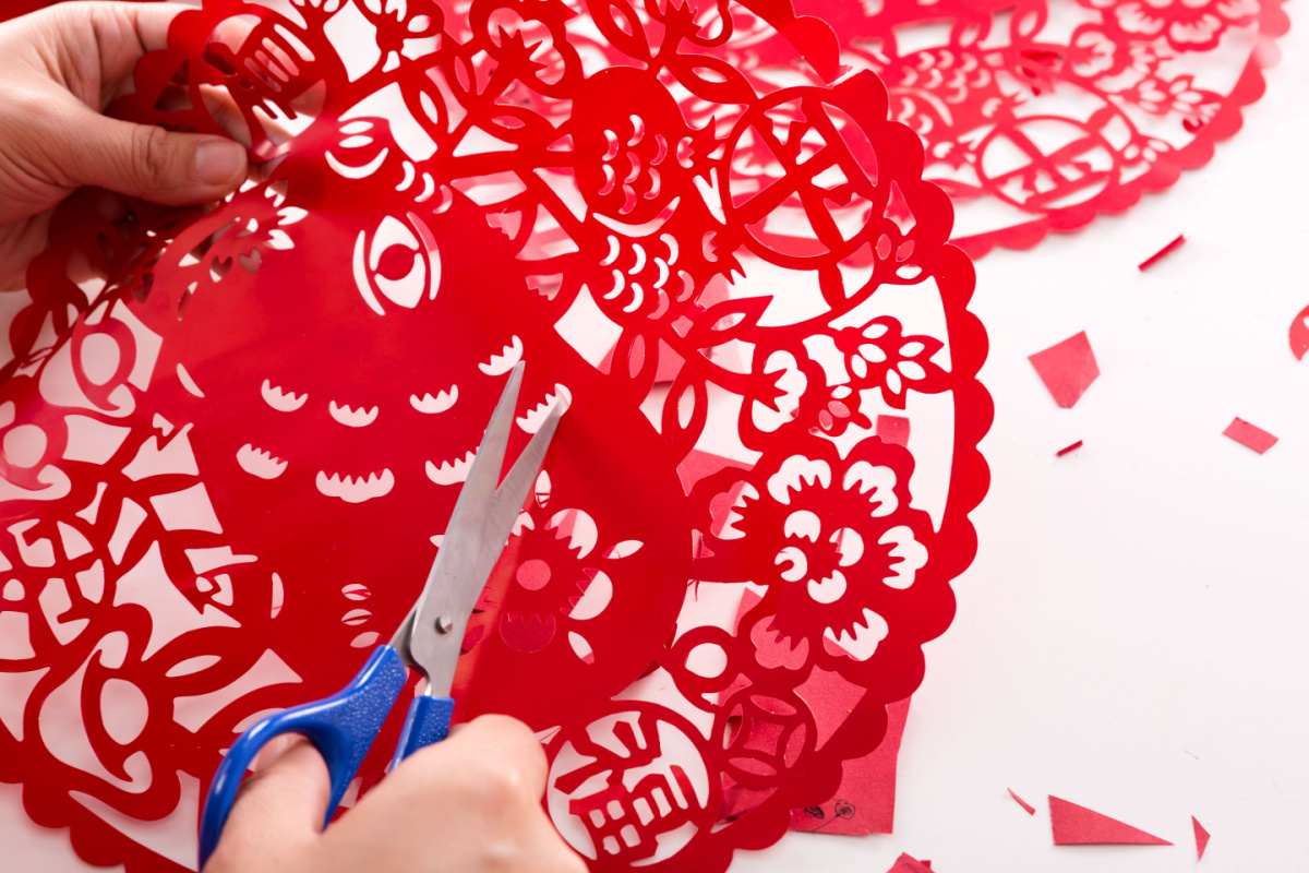 Chinese New Year paper cuttings A Chinese New Year paper cutting of a lucky fish being cut by a right handed person with a blue scissors.