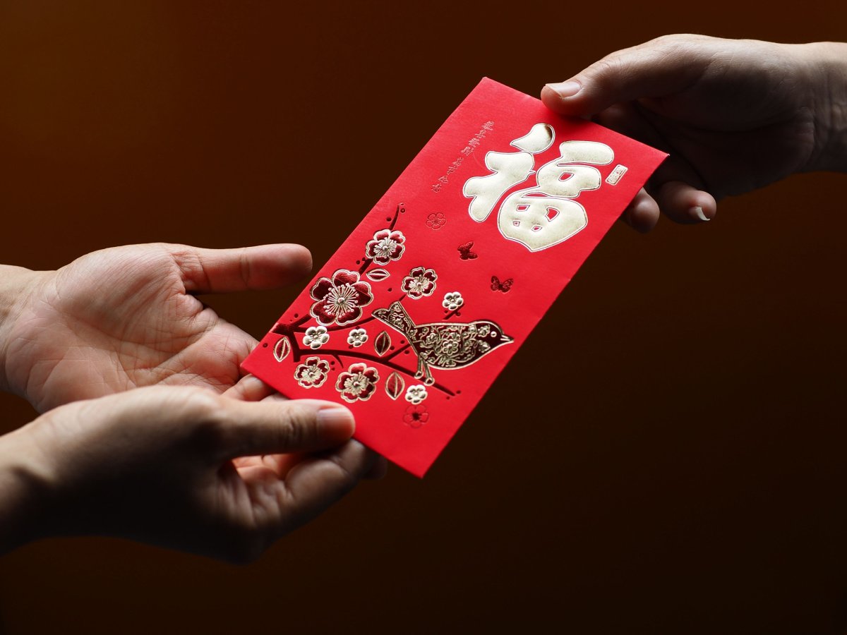Red envelope being gifted A person handing a Chinese New Year red envelope with a bird and the fu character on it to another person who is accepting it with both hands.