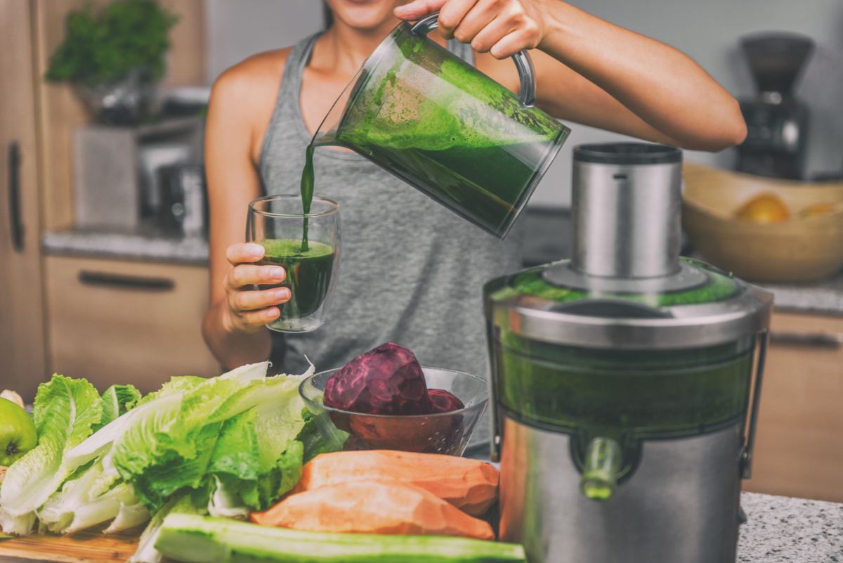 Woman pouring green juice A woman wearing a grey tank top pouring green juice into a glass for National Green Juice Day, with a used juicer, green apples, romaine lettuce, peeled sweet potatoes, beets and cucumbers in the foreground of the image.
