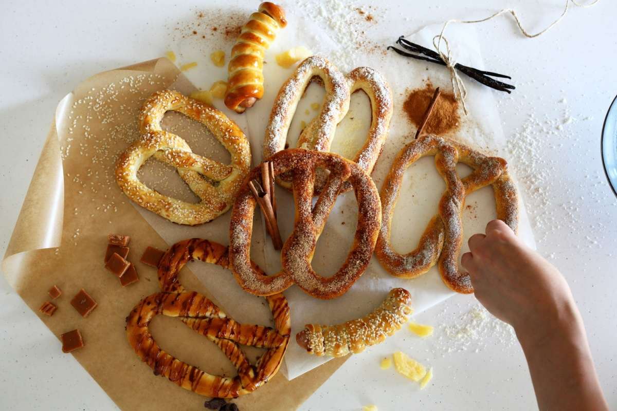 Various types of pretzels Various types of pretzels arranged on a cloth which is on top of a white surface, and a hand is grabbing one of the soft pretzels to the far left of the image.