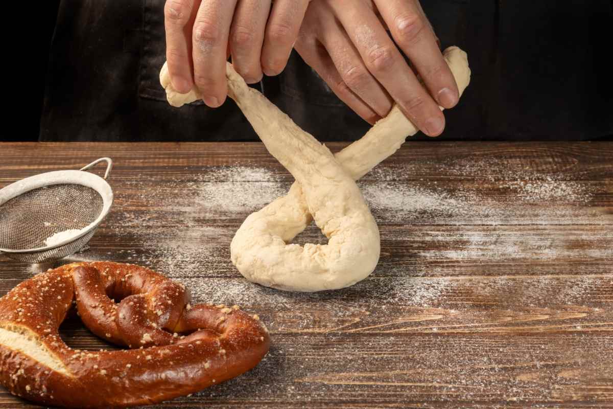 Hands shaping a pretzel A close up image of two hands shaping a homemade pretzel into a pretzel shape on a floured wooden surface next to an already baked pretzel.