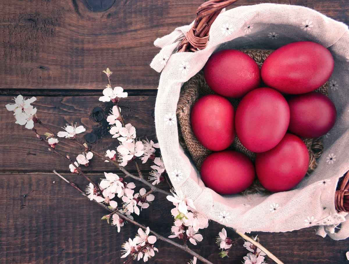 Red Easter eggs A wooden background with a wicker basket lined with light pink linen with eyelets in it, with seven red Easter eggs on it, next to a branch of dogwood flowers, both of which are Easter symbols.