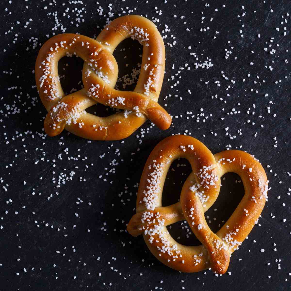 Two pretzels on a black background Two homemade pretzels on a black background that is filled with grains of salt.