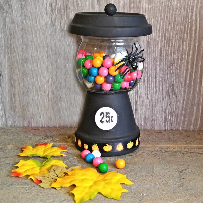 Halloween gumball machine craft made from terra cotta pots and filled with bubblegum sitting near two yellow leaves.