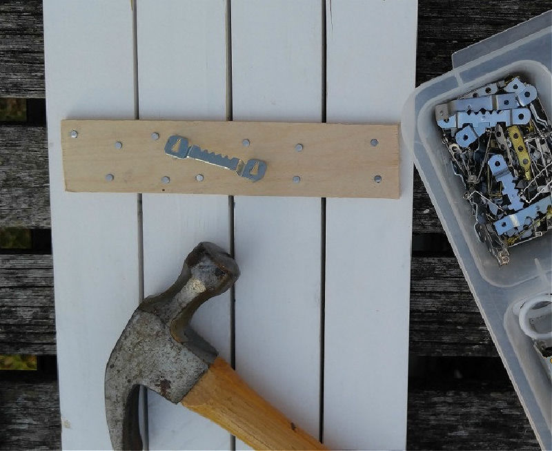 Metal sawtooth hanger on a piece of wood with hammer and other hangers in a plastic case.