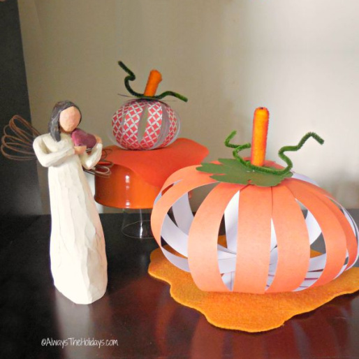 Two DIY paper pumpkins displayed on a mahogany wood table beside an angel figure.