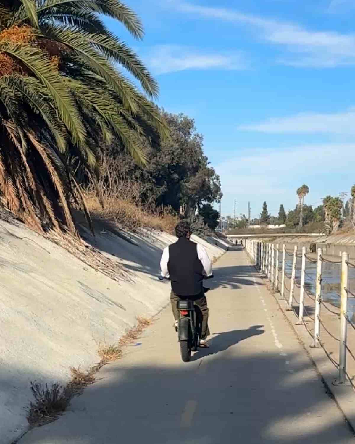 Bike riding A man riding an electric bike on the Ballona Creek Bike Path with palm trees to his left and the creek to his right.
