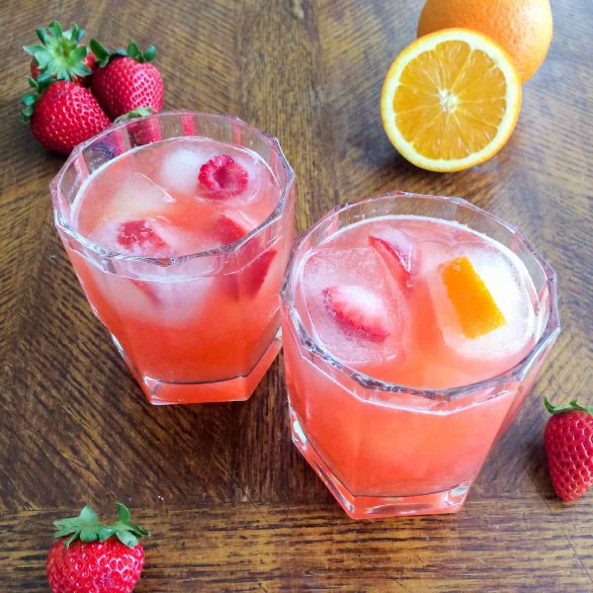 Tropical mocktail Two glasses filled with tropical mocktails for summer, with fruit ice cubes in the glasses, and fresh strawberries and oranges arranged on the table around the glasses.
